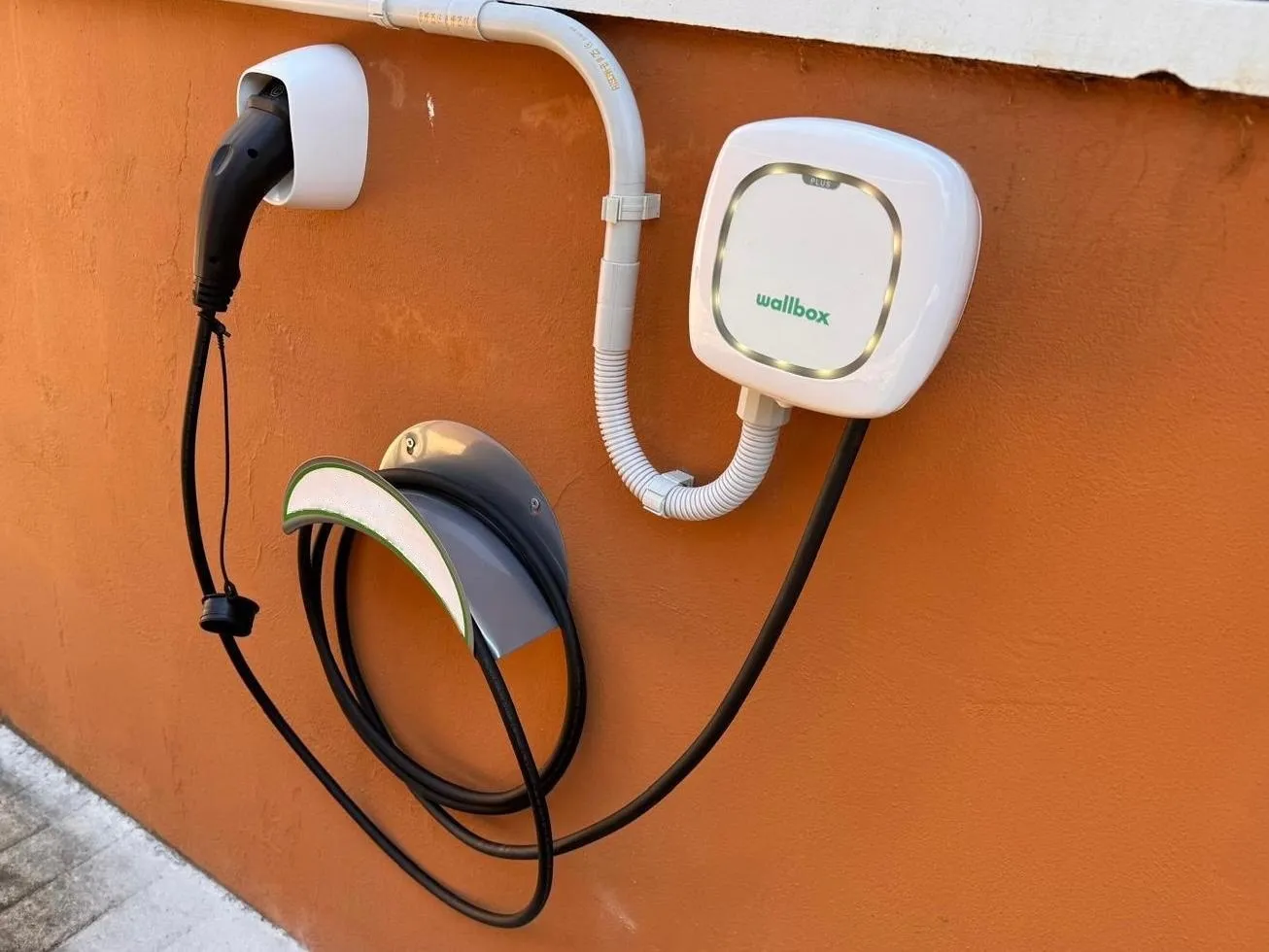 Punto de recarga doméstico instalado en la pared de una casa con el cable recogido en su soporte