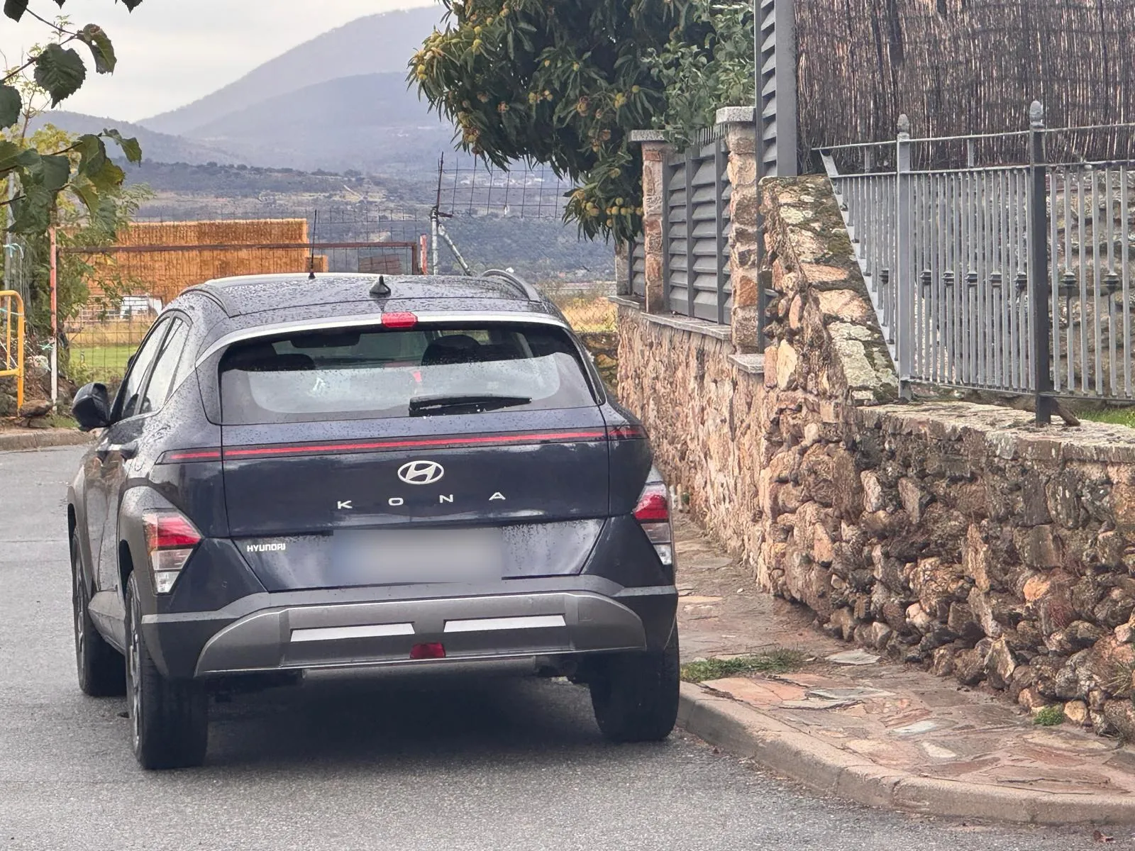 Trasera del Hyundai KONA XLS azul con la franja de pilotos LED y las montañas de la Sierra Norte de Madrid al fondo