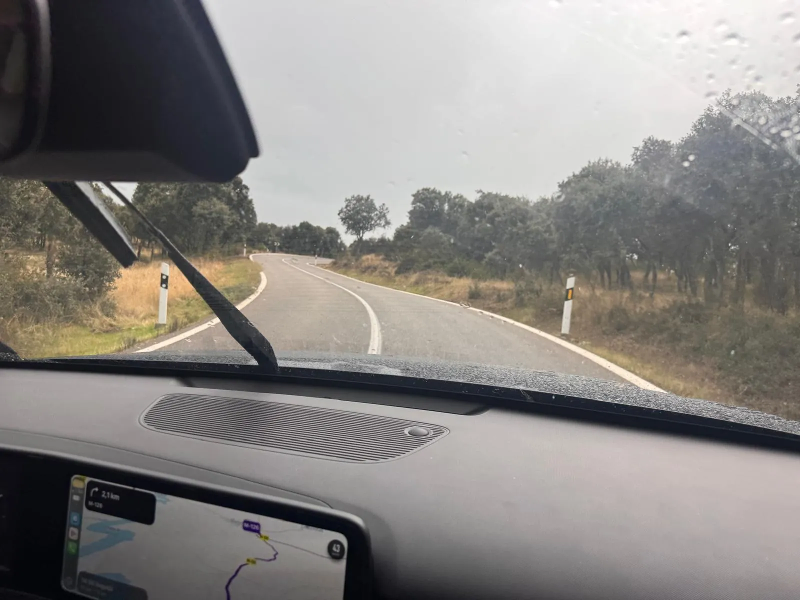 Carretera de montaña estrecha y mojada con curvas en la Sierra Norte de Madrid vista desde el interior del Hyundai KONA